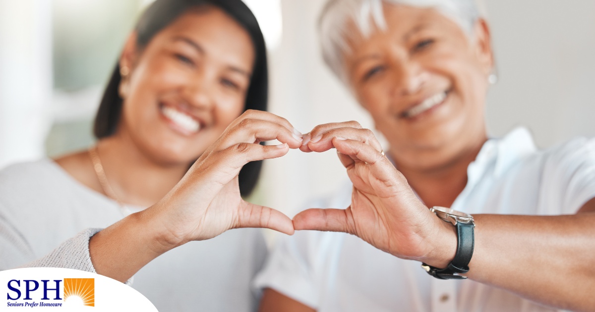 A daughter and an older mother create a heart with their hands, representing the feeling that is highlighted during National Family Caregivers Month