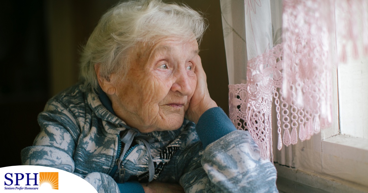 An older woman peacefully looks out of the window while the sun is still up, representing what can happen with sundowning.